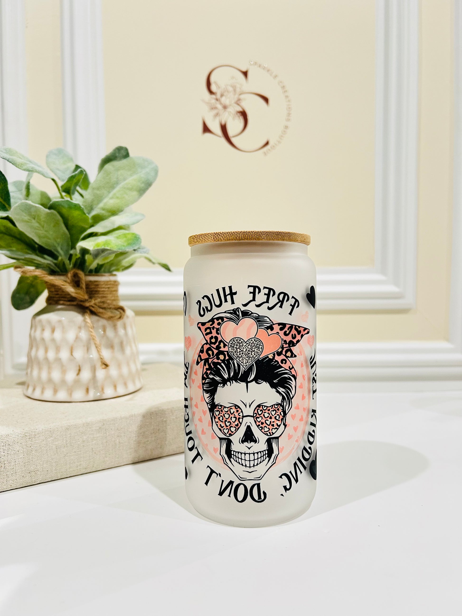 Decorative jar with skull design and text on a white surface with a plant in the background
