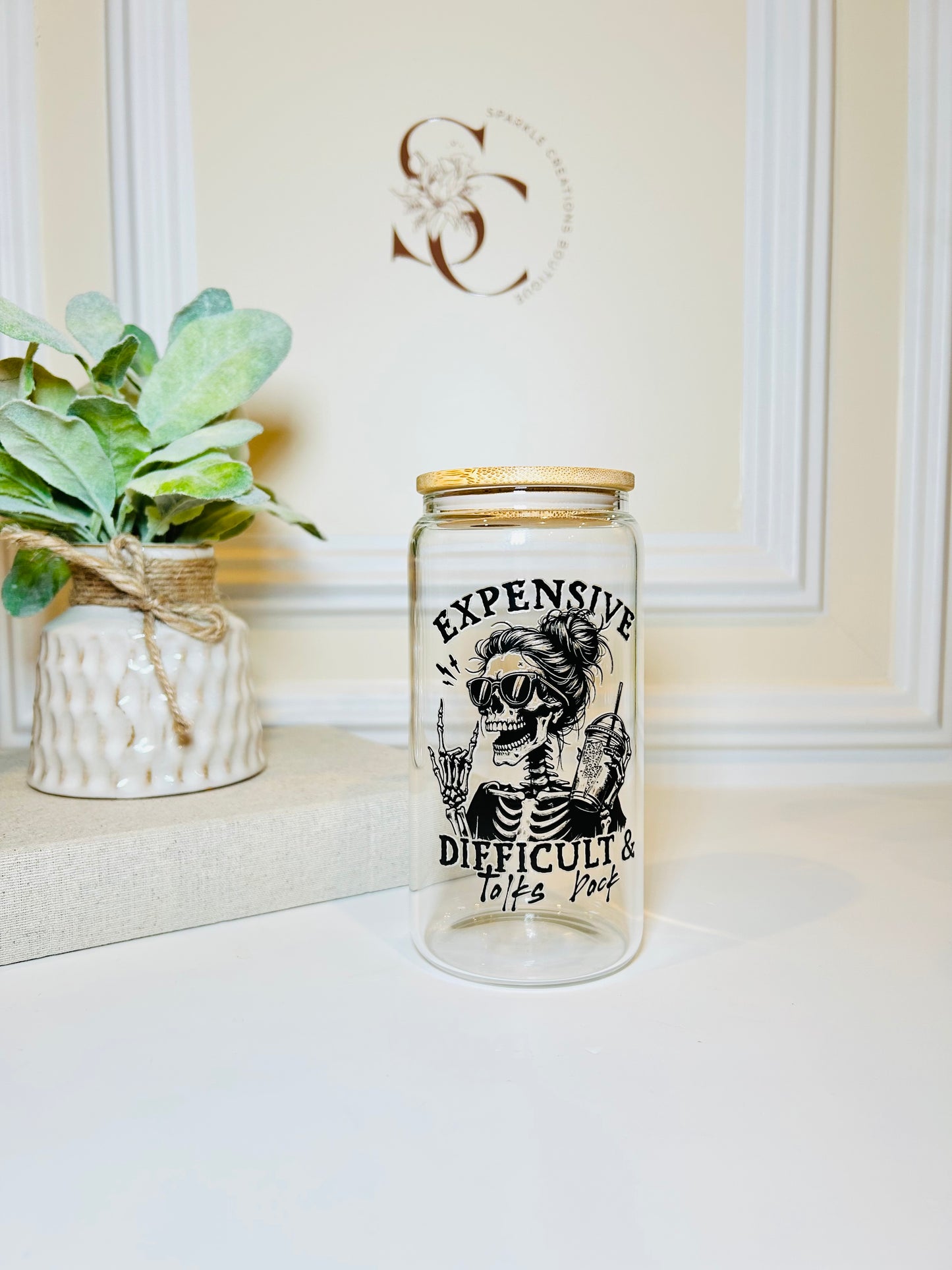 Glass jar with a skeleton design and text on a white surface with a plant in the background.