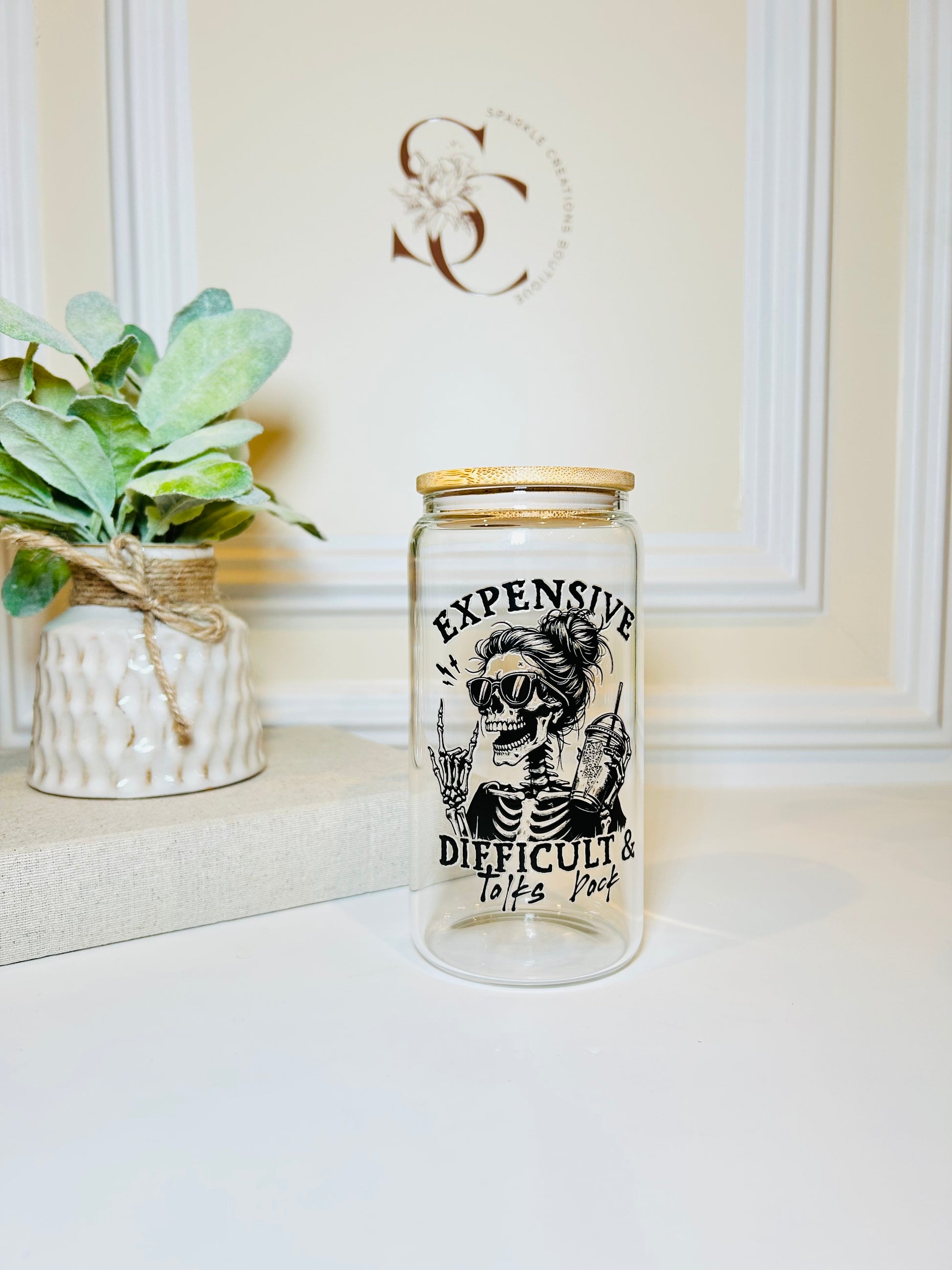 Glass jar with a skeleton design and text on a white surface with a plant in the background.