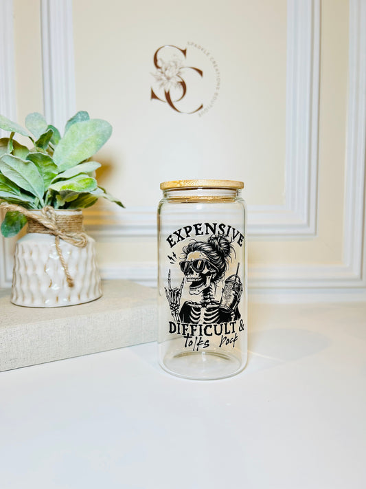 Glass jar with a skeleton design and text on a white surface with a plant in the background.